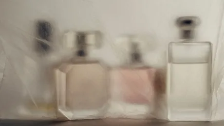 Olfaktorni simyi povnyy putivnyk vid tsytrusovykh do udu Blurry image of three perfume bottles on a white surface seen through a sheer fabric curtain.