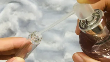 Shcho take dekant i chomu tse nayrozumnishyy sposib kupuvaty nishevu parfumeriyu Two hands transfer liquid from a small dropper bottle into a brown glass bottle using a glass pipette.