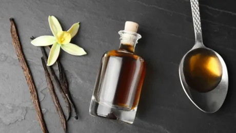 Top-10 nishevykh aromativ z notamy vanili vid Le Labo do MFK Vanilla beans, a yellow orchid, and a bottle of vanilla extract on a dark slate surface.