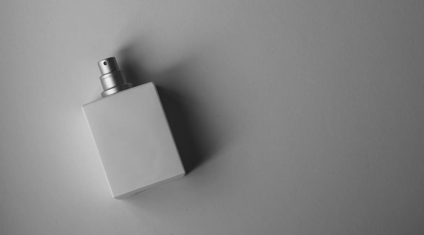 Parfumy yak bilyy shum akordy dlya tykh, khto shukaye minimalizm White square perfume bottle with a silver spray nozzle resting on a neutral surface.