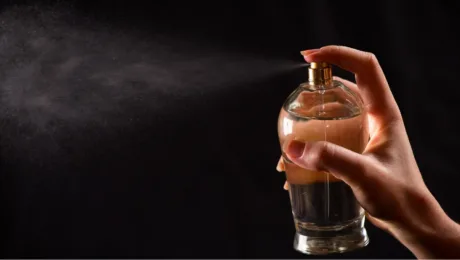 Muskusni aromaty chomu parfumy z efektom shkiry stayut holovnym trendom nishevoyi parfumeriyi Hand pressing a perfume spray bottle, releasing a fine mist against a dark background.